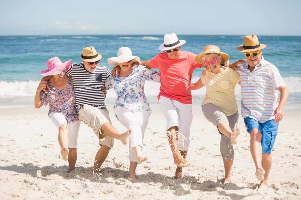 Seniors in a line kicking up their legs in the sand on the beach