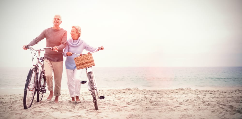 A senior man and a senior woman walking their bikes on the beach