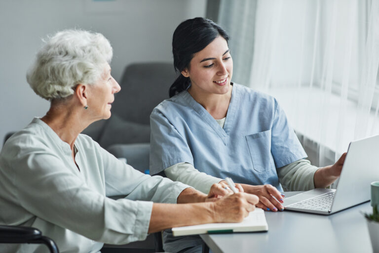 Portrait of smiling female caregiver helping senior woman using laptop at home, copy space