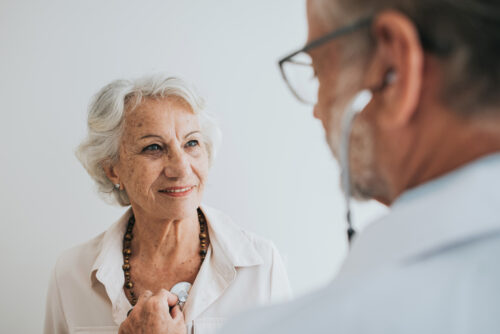 Doctor listening to senior woman patient heartbeat