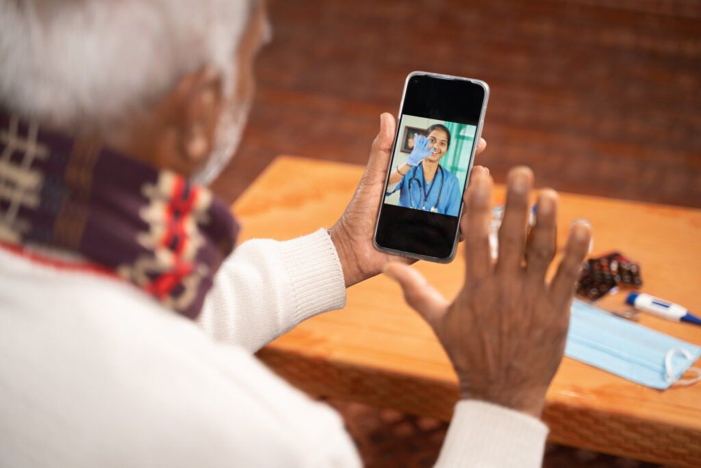 Shoulder shot of Old man on video with to doctor on mobile phone - concept of nurse Online Chat, telehealth, or tele counseling during coronavirus or covid-19 pandemic.