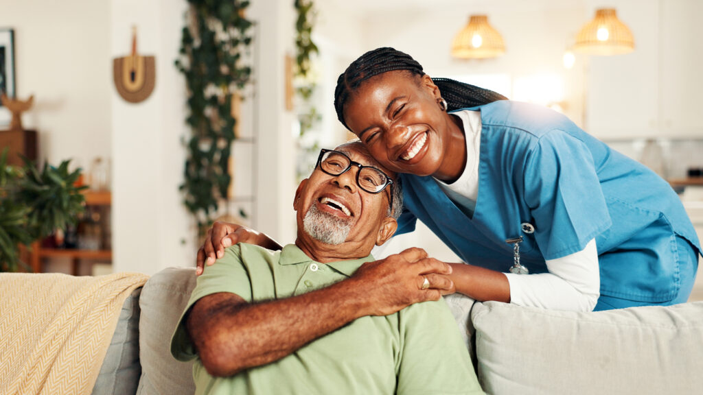 Hugging, happy and nurse with senior man for comfort, support or care for good news. Portrait, consultation and caregiver embracing elderly male patient on sofa in living room at nursing home.