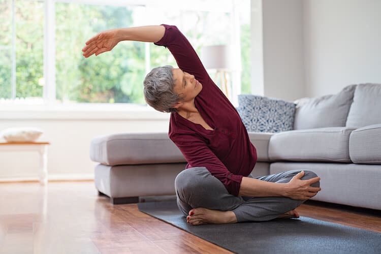 Senior woman sitting on yoga mat stretching