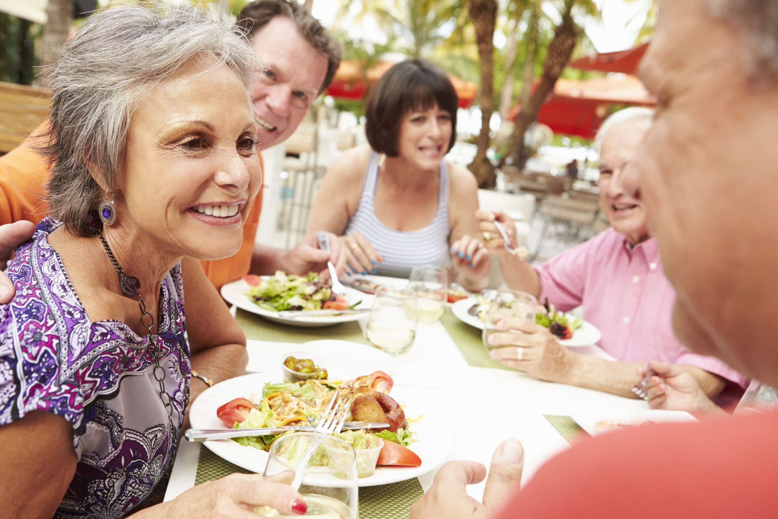 A group of senior friends eats dinner together on a patio