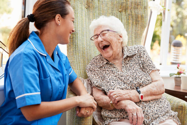 Senior Woman Sitting In Chair And Laughing With Nurse
