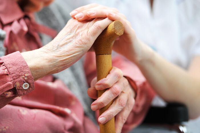 Younger nurse holding hand of older woman in hospice care